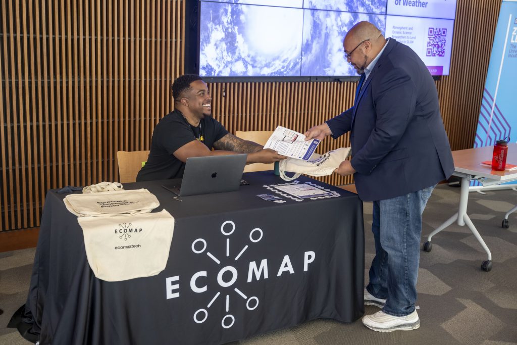 Photo of Ecomap sponsor table at a past event, with an attendee getting information from the person at the table