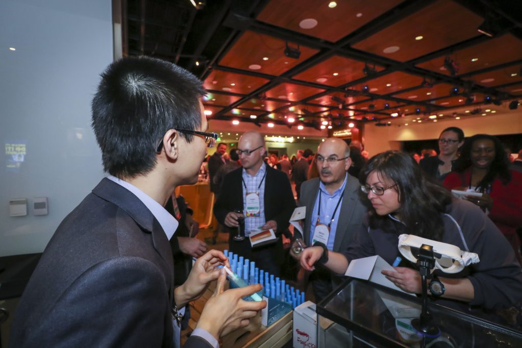 Photo of a sponsor booth at a past event, with attendees crowded around talking to the person at the table